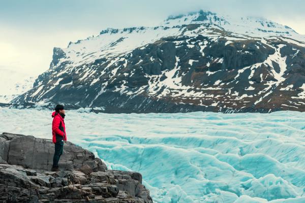 a man in a red jacket is standing on a rock overlooking a glacier in Iceland