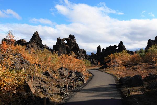 Winding path through dark volcanic landscape with vibrant autumn foliage and a natural rock arch.