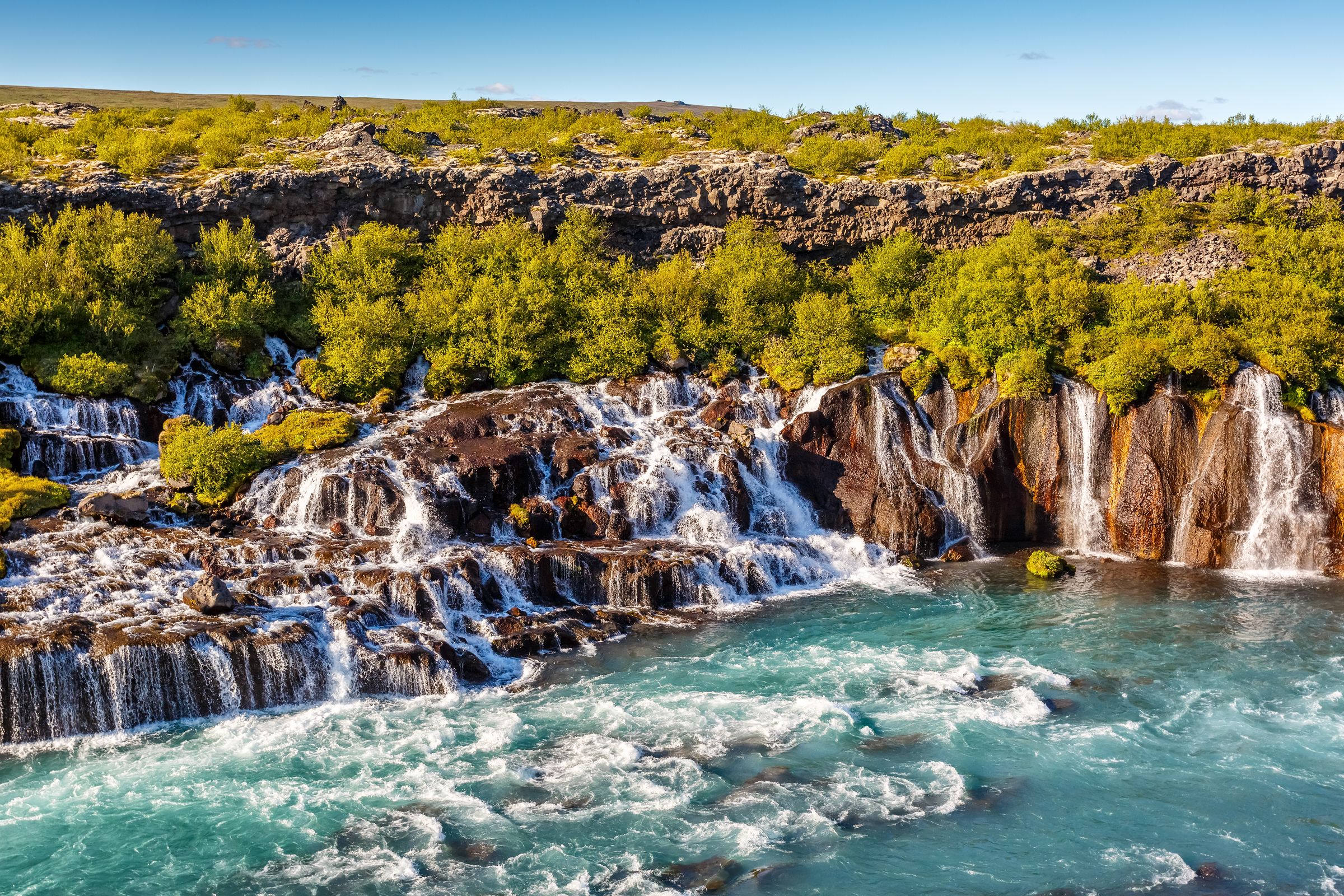 an aerial view of a waterfall in the middle of a river surrounded by trees at Hraunfossar in Iceland.