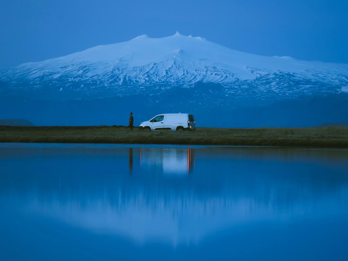Spiegelung eines kompakten Wohnmobils im Wasser Ein kompakter Campervan für 2 Personen am Wasser, in dem sich ein großer Berg spiegelt, Campervan-Vermietung Island