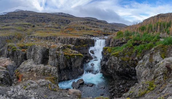 a waterfall in the middle of a canyon surrounded by rocks and trees .