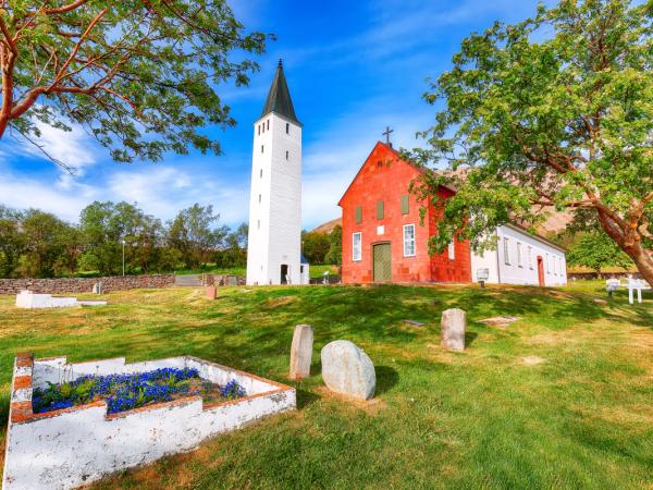 A vibrant red church building with a tall white bell tower in a green graveyard under a bright blue sky.