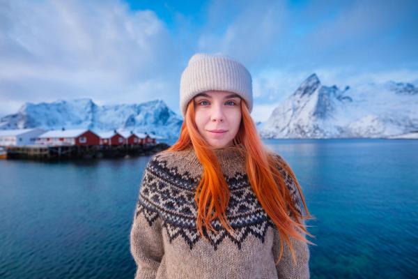 una mujer con un suéter y un sombrero está de pie frente a un lago .