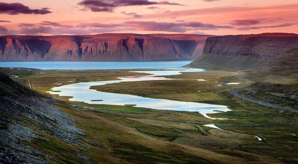 a river flowing through a valley surrounded by mountains at sunset at westfjords in iceland.