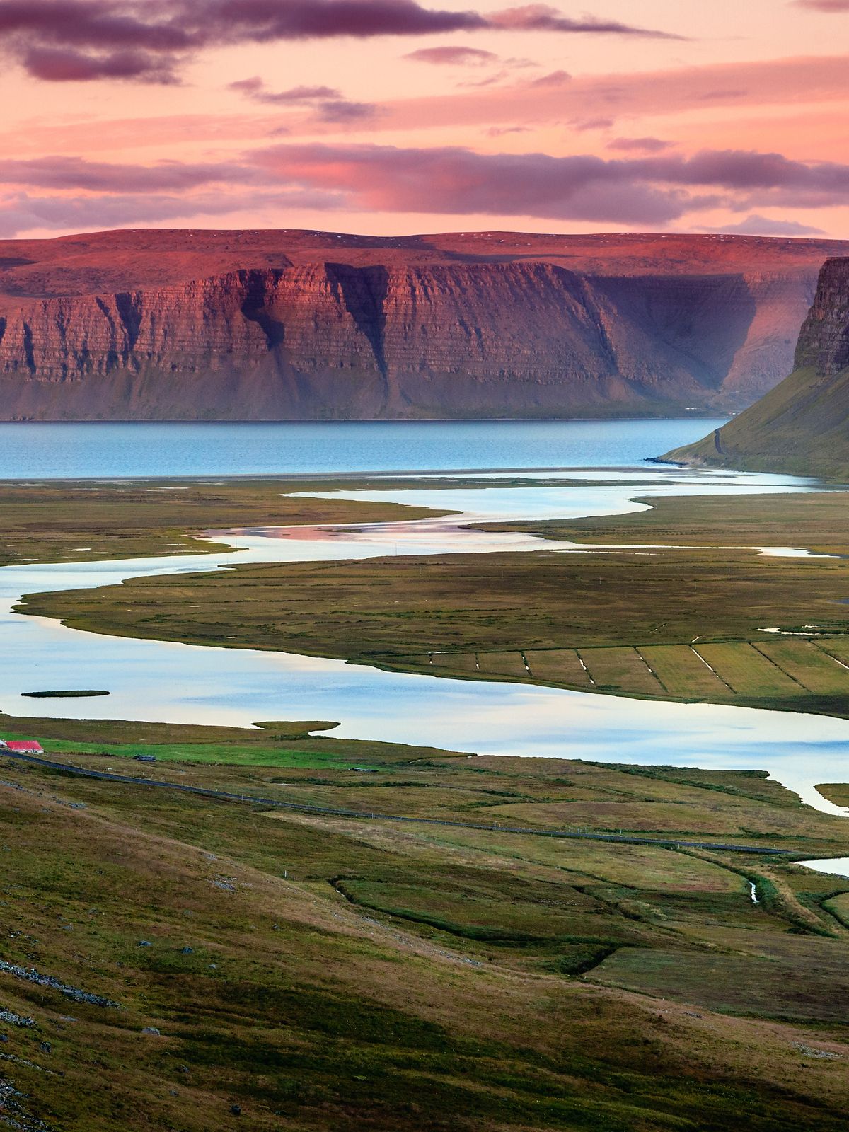 a river flowing through a valley surrounded by mountains at sunset at westfjords in iceland.