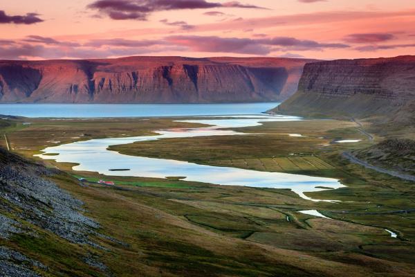 a river flowing through a valley surrounded by mountains at sunset .