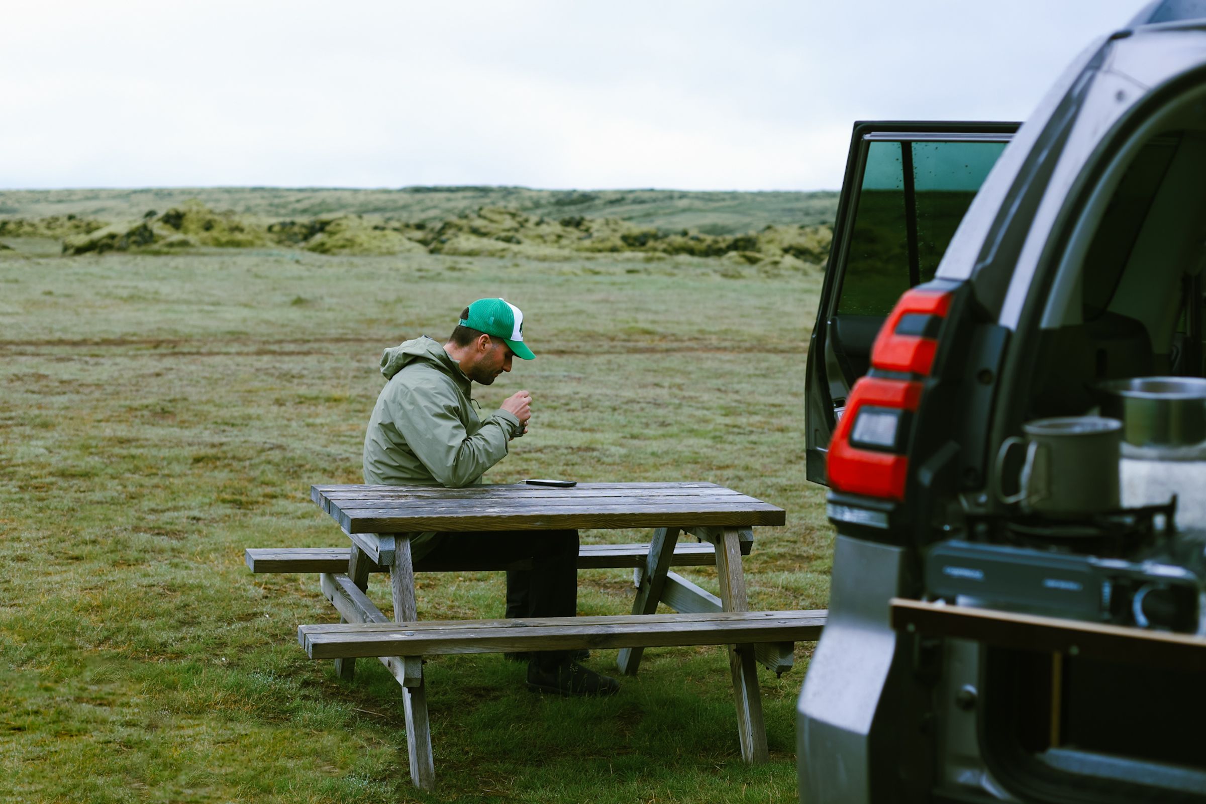 Manneskja við lautarborð við hliðina á opnu afturhleranum, með krúsir á eldhúshillunni