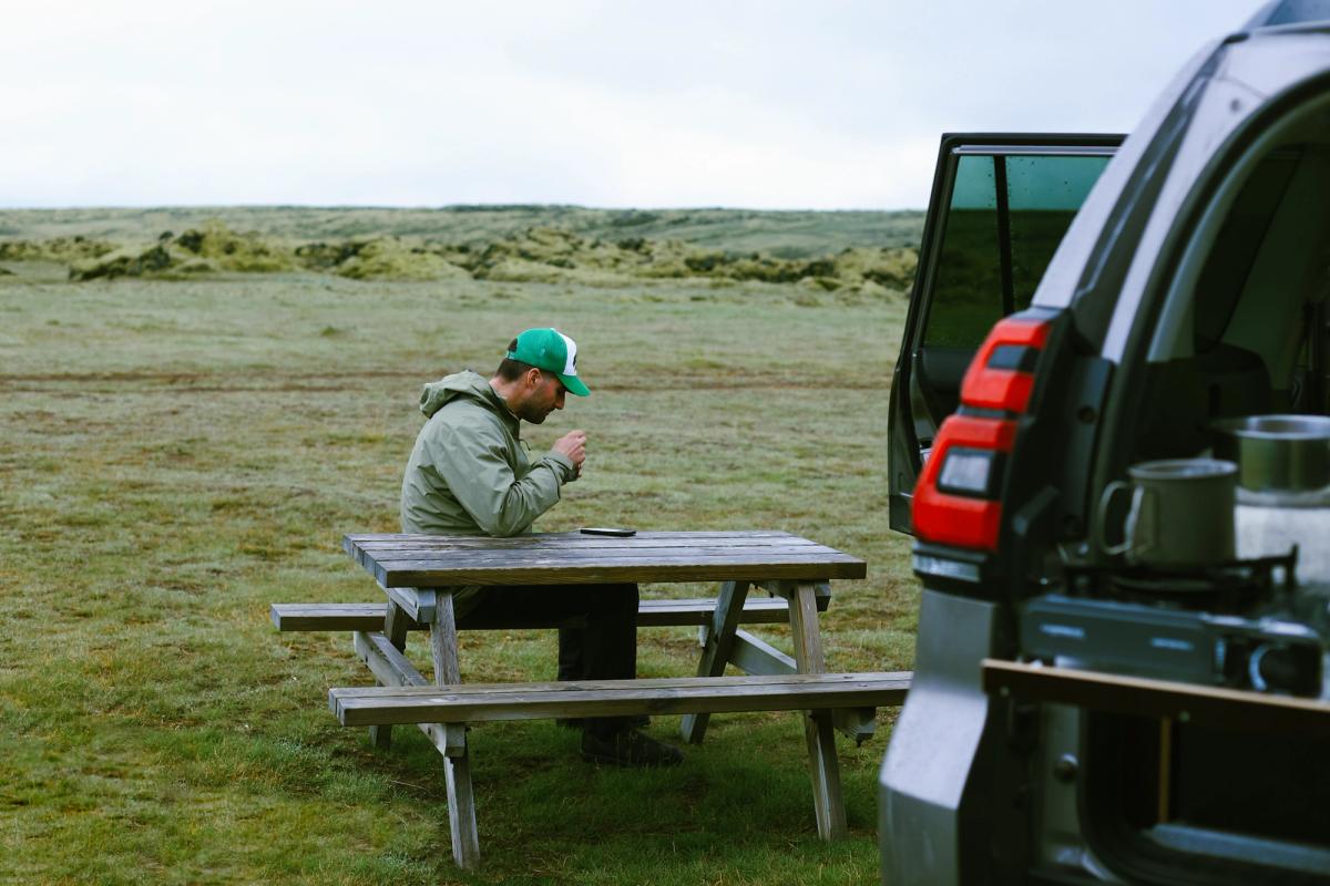 Manneskja við lautarborð við hliðina á opnu afturhleranum, með krúsir á eldhúshillunni
