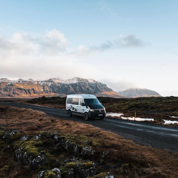 a white van is driving down a road with mountains in the background .