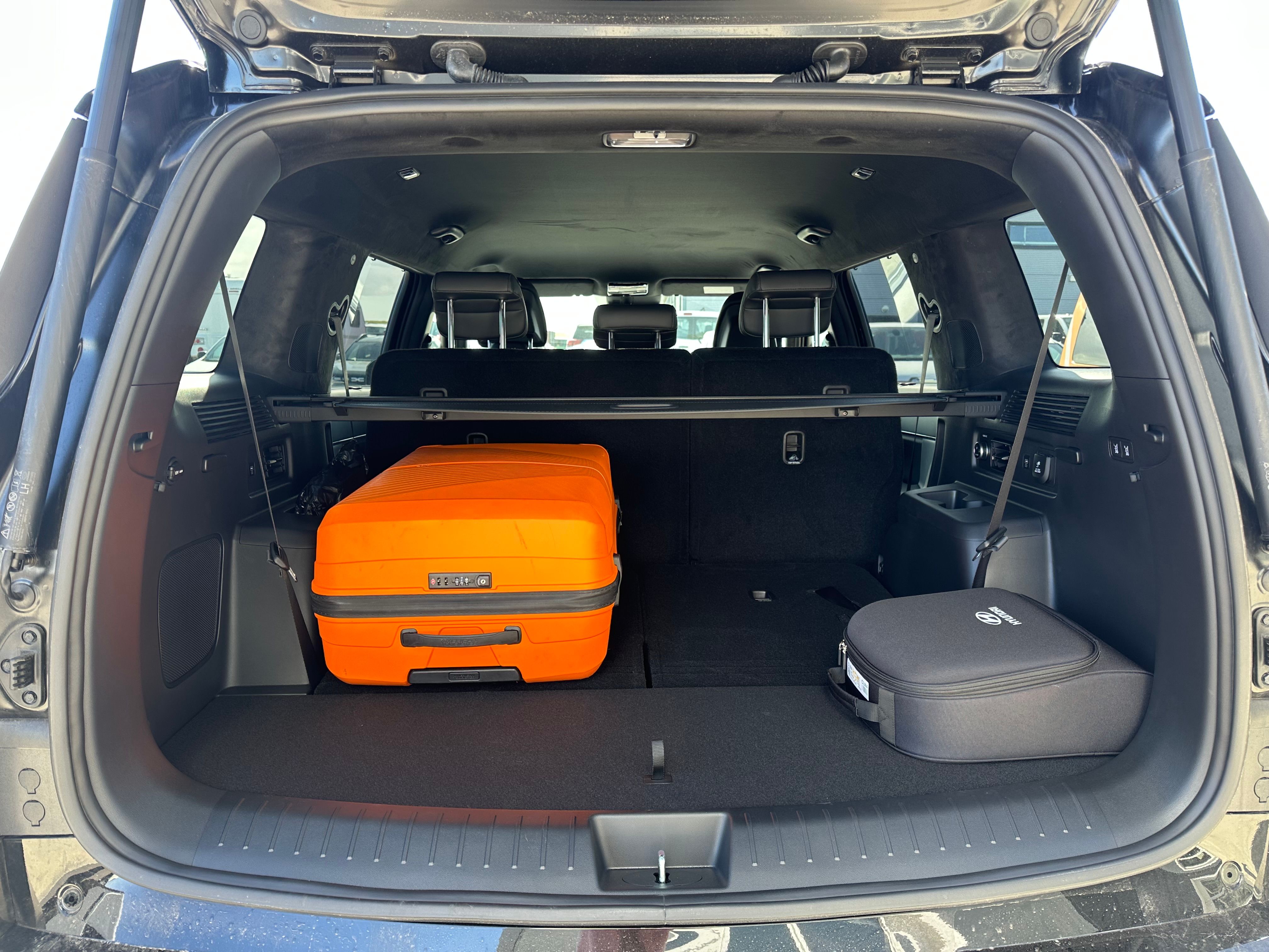 Open car trunk showing an orange suitcase and a black bag.