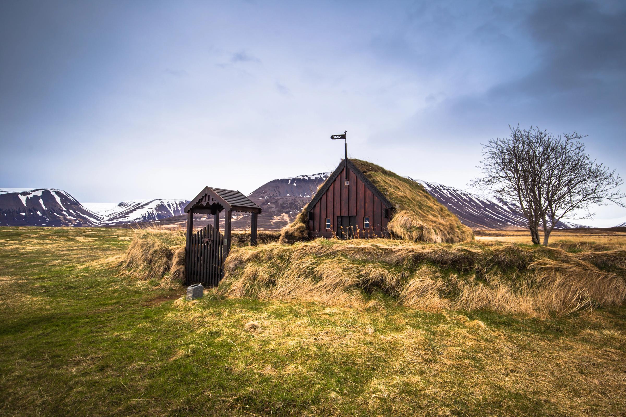 a small house with a grass roof is sitting on top of a hill in a field .