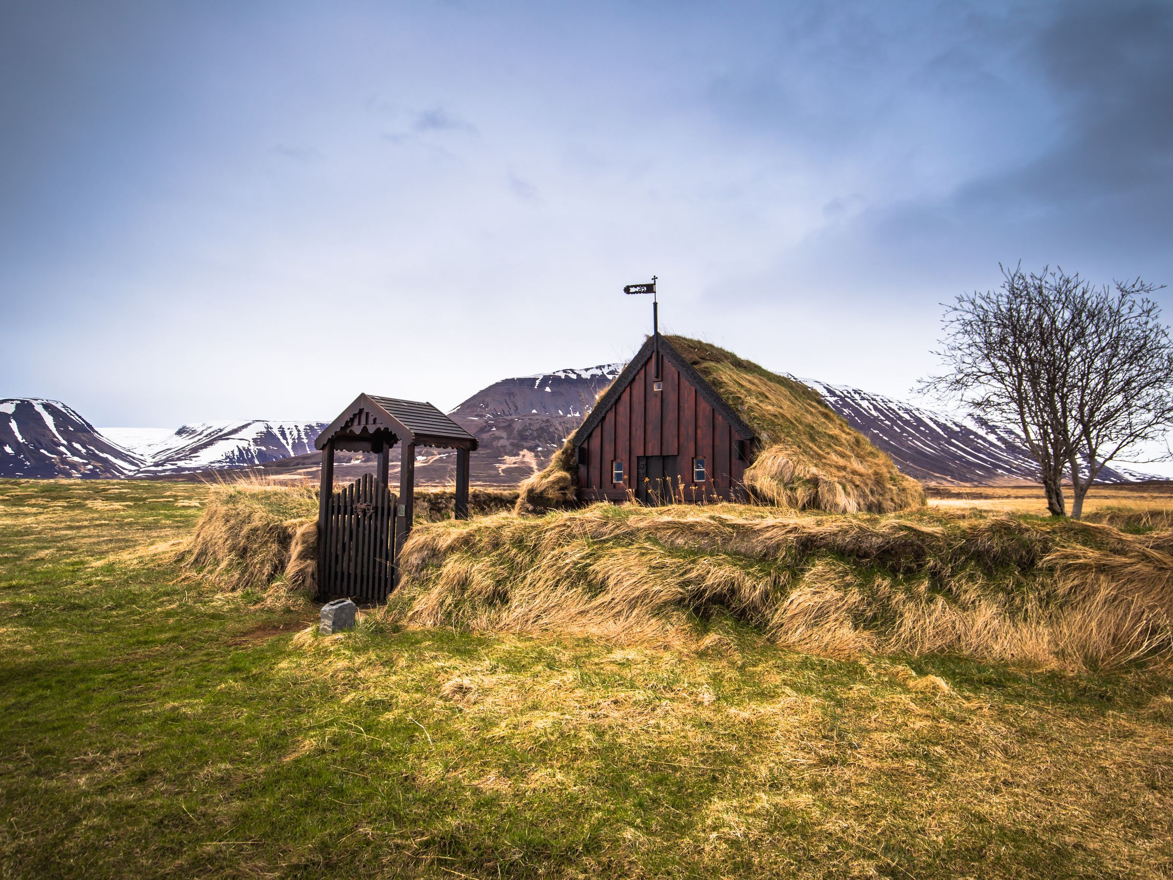 a small house with a grass roof is sitting on top of a hill in a field .