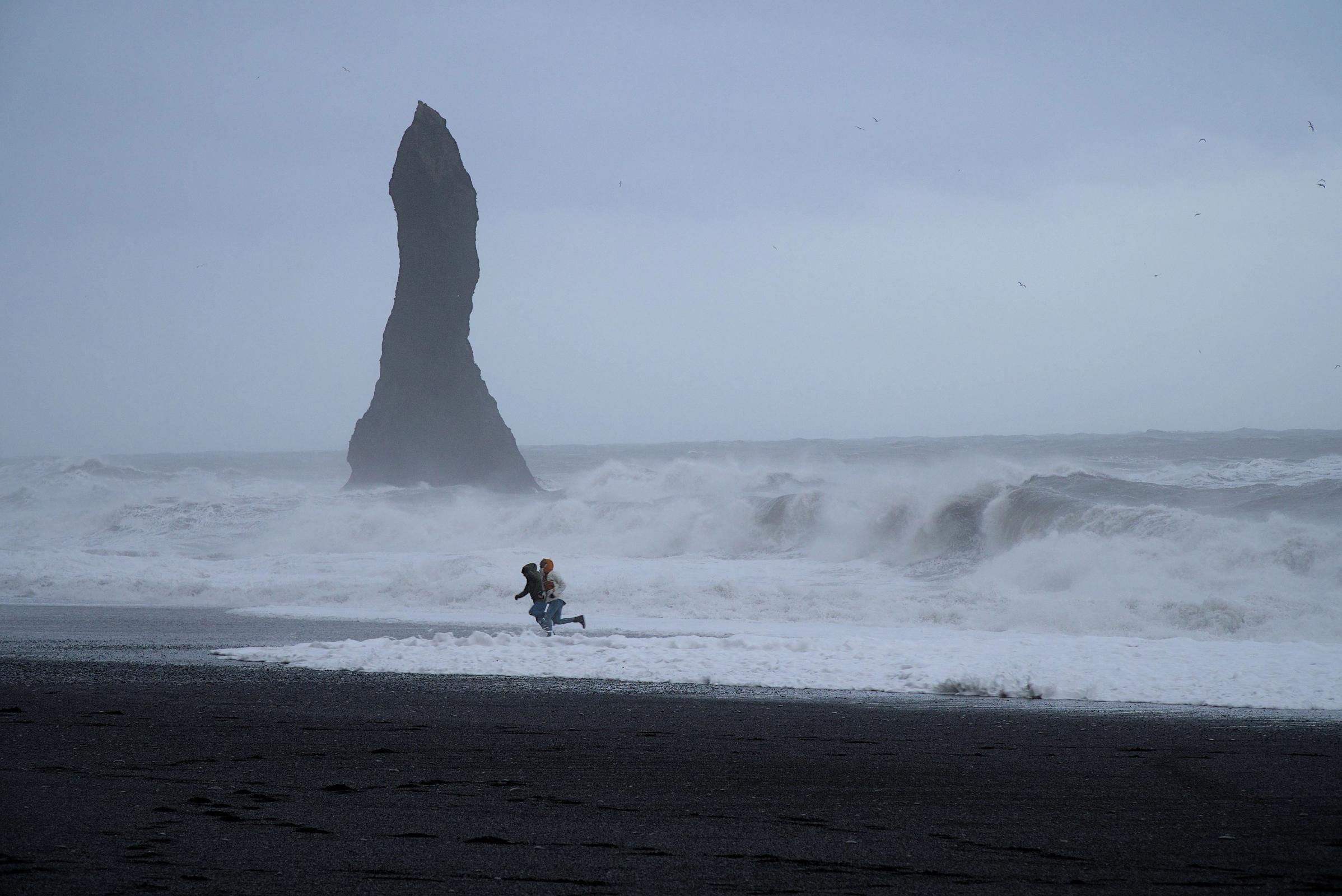 Dos personas corriendo para escapar de las sneaker waves en Reynisfjara