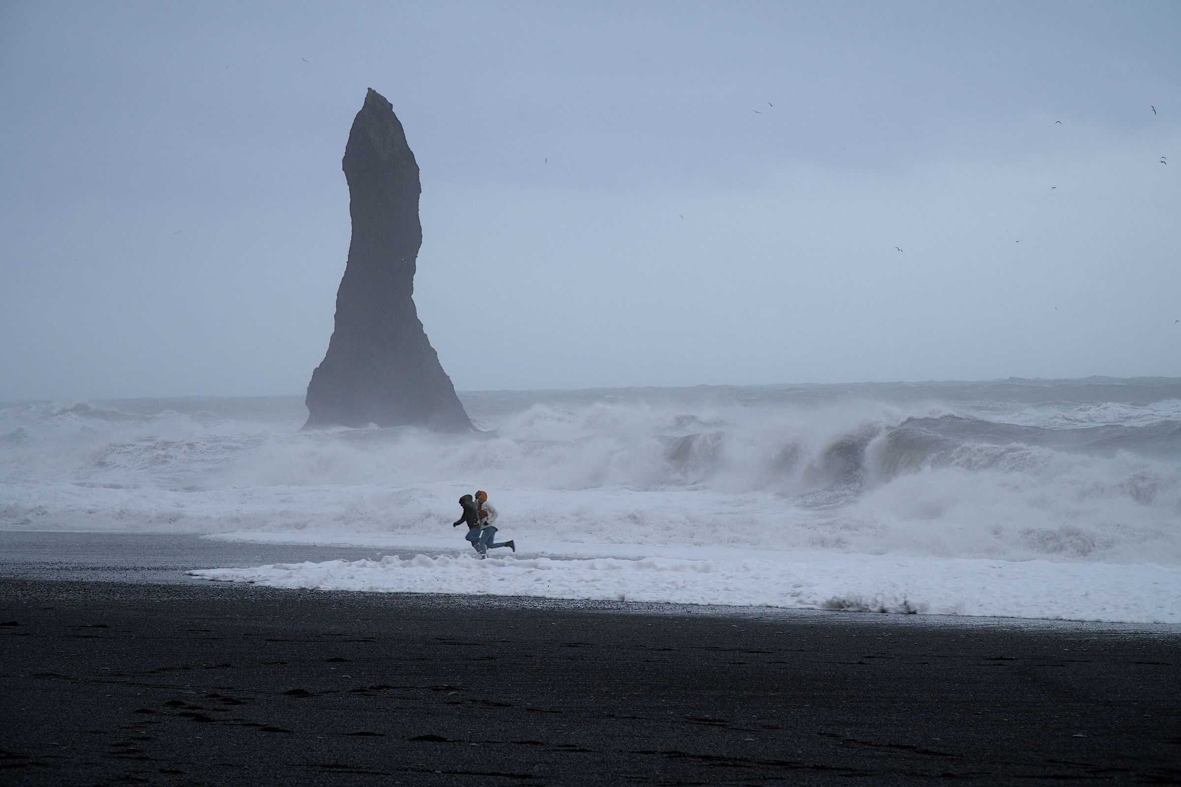 Dos personas corriendo para escapar de las sneaker waves en Reynisfjara