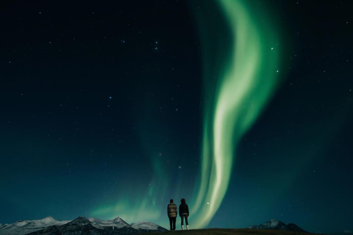 Couple admiring aurora borealis in the blue and starry sky of iceland in winter time 