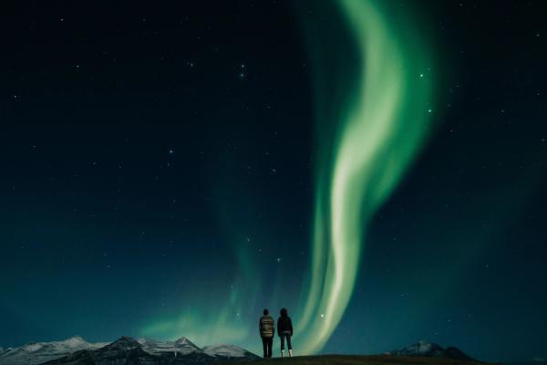 Pareja admirando la aurora boreal en el cielo azul y estrellado de Islandia en pleno invierno