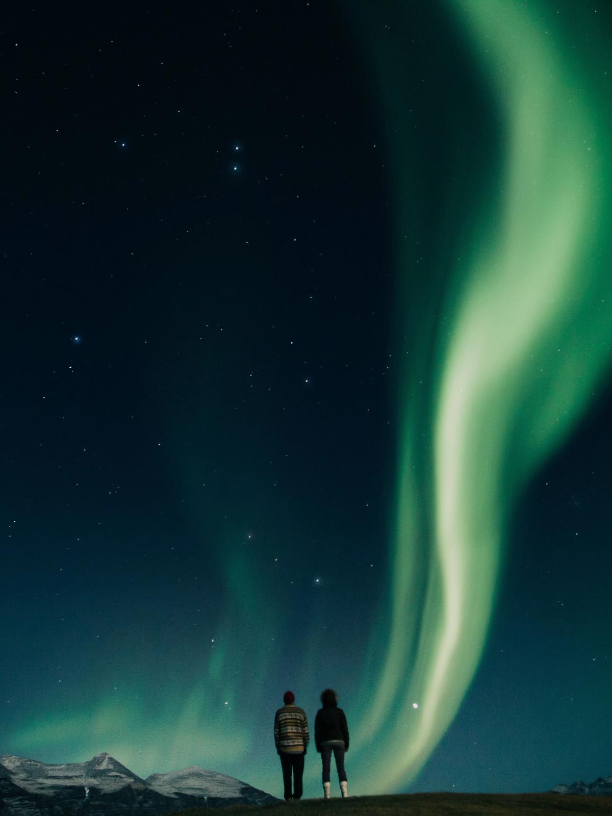Couple admiring aurora borealis in the blue and starry sky of iceland in winter time