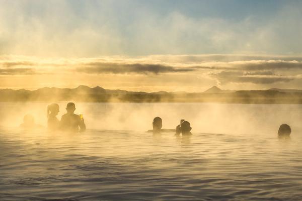 a group of people are swimming in a hot spring at sunset in iceland.