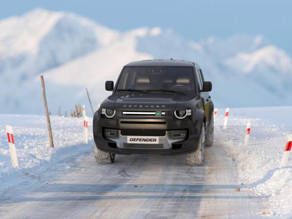 Dark Land Rover Defender SUV driving on a snowy mountain road.