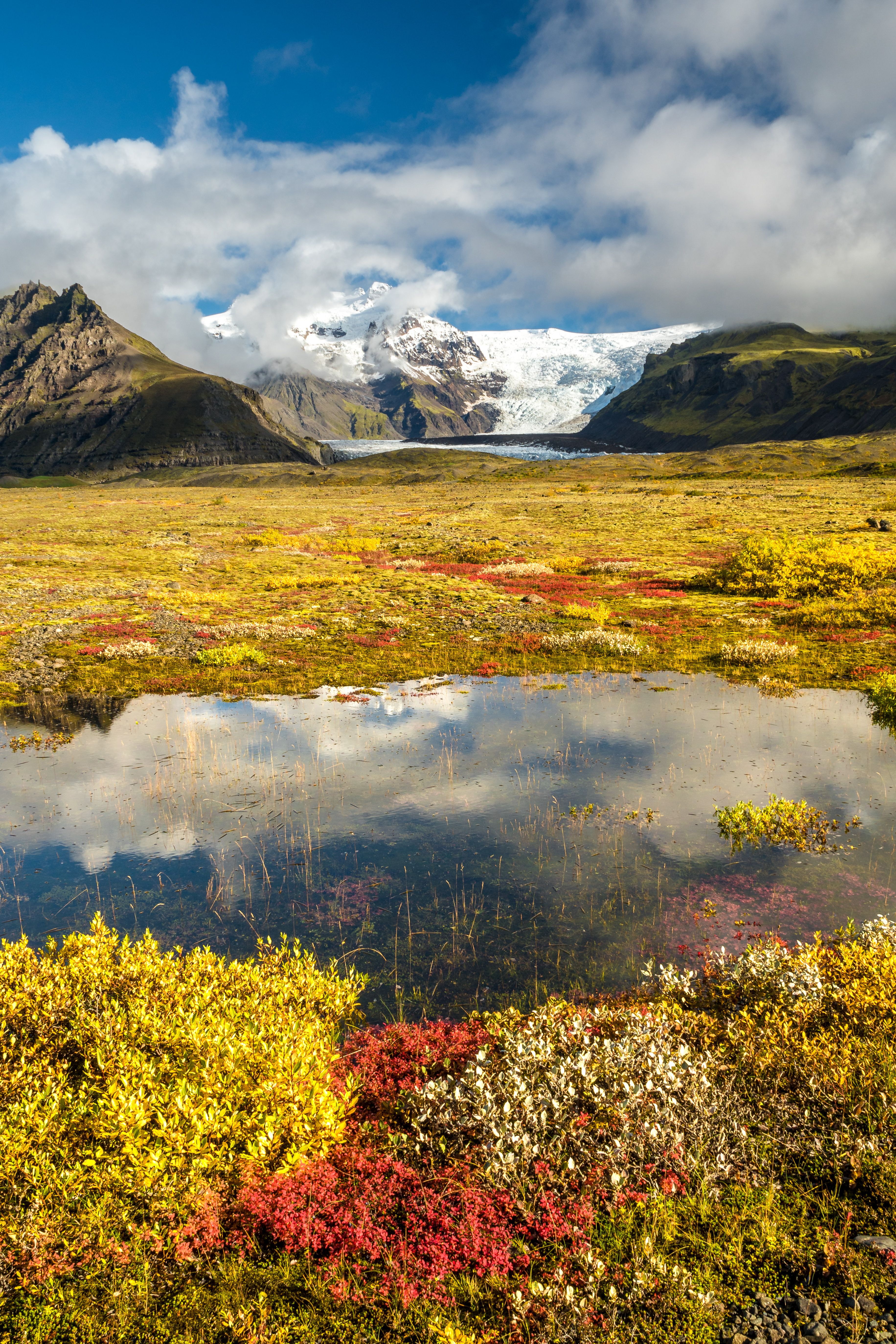 a lake in the middle of a field with mountains in the background