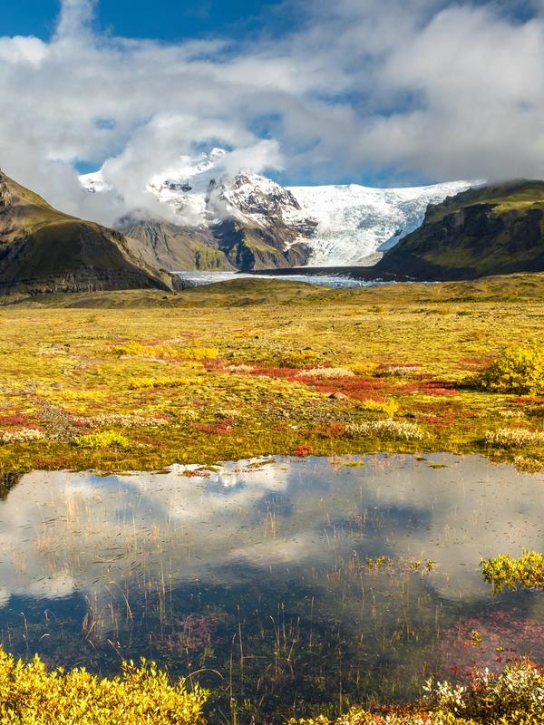 a lake in the middle of a field with mountains in the background