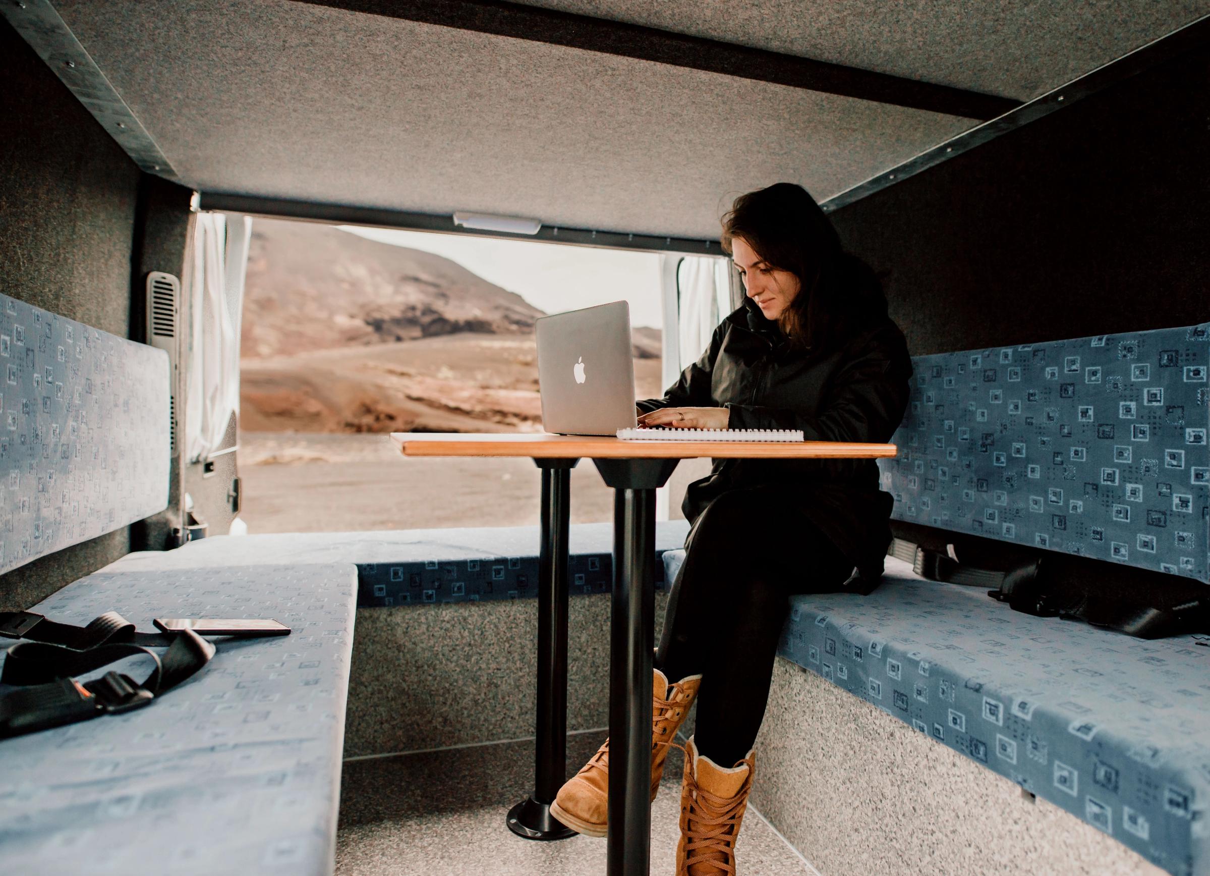 Person mit Laptop am Esstisch, Seitentür mit Blick auf eine Berglandschaft geöffnet