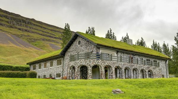 una casa de piedra con techo verde se encuentra en medio de un campo cubierto de hierba.