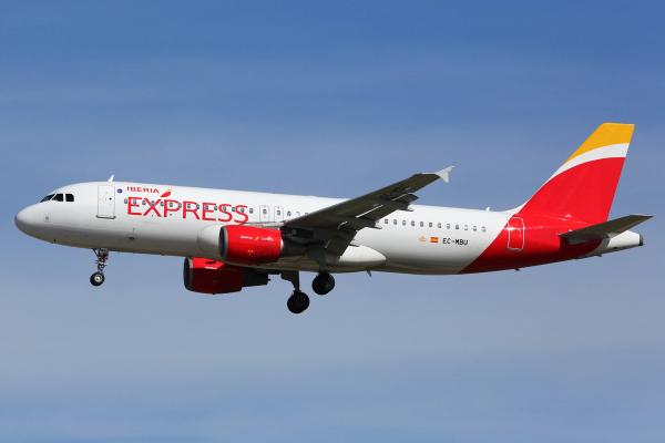 White Iberia Express airplane flying with landing gear extended against a blue sky.