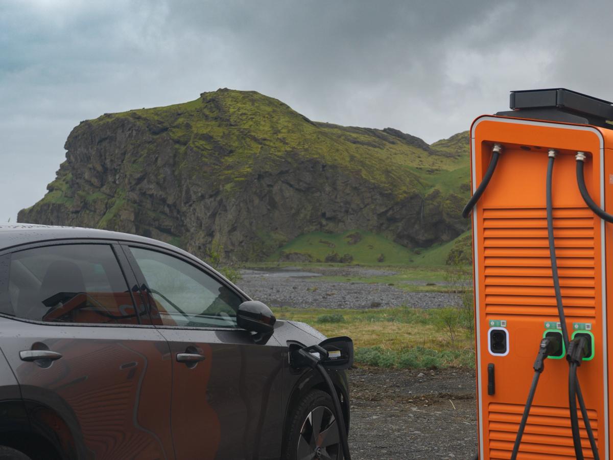 Hleðslustöð fyrir Nissan Ariya Nissan Ariya rafbíll í hleðslu við hleðslustöð með græna hæð í bakgrunni