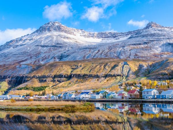 A village with colorful houses reflected in water, backed by snow-dusted mountains under a blue sky.