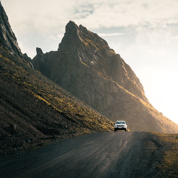 A white SUV on a gravel road winding through rugged, sunlit mountains.