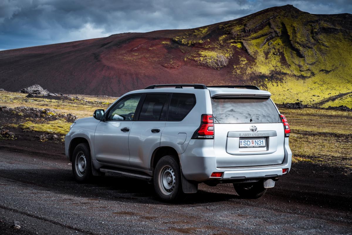 Toyota Land Cruiser seen from the rear side on a gravel track below a mossy slope