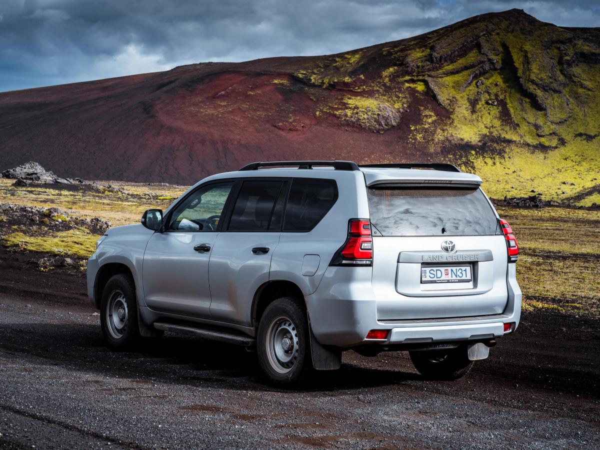 Land Cruiser Schotterpiste Toyota Land Cruiser von schräg hinten auf einem Schotterweg unterhalb eines moosbewachsenen Hangs