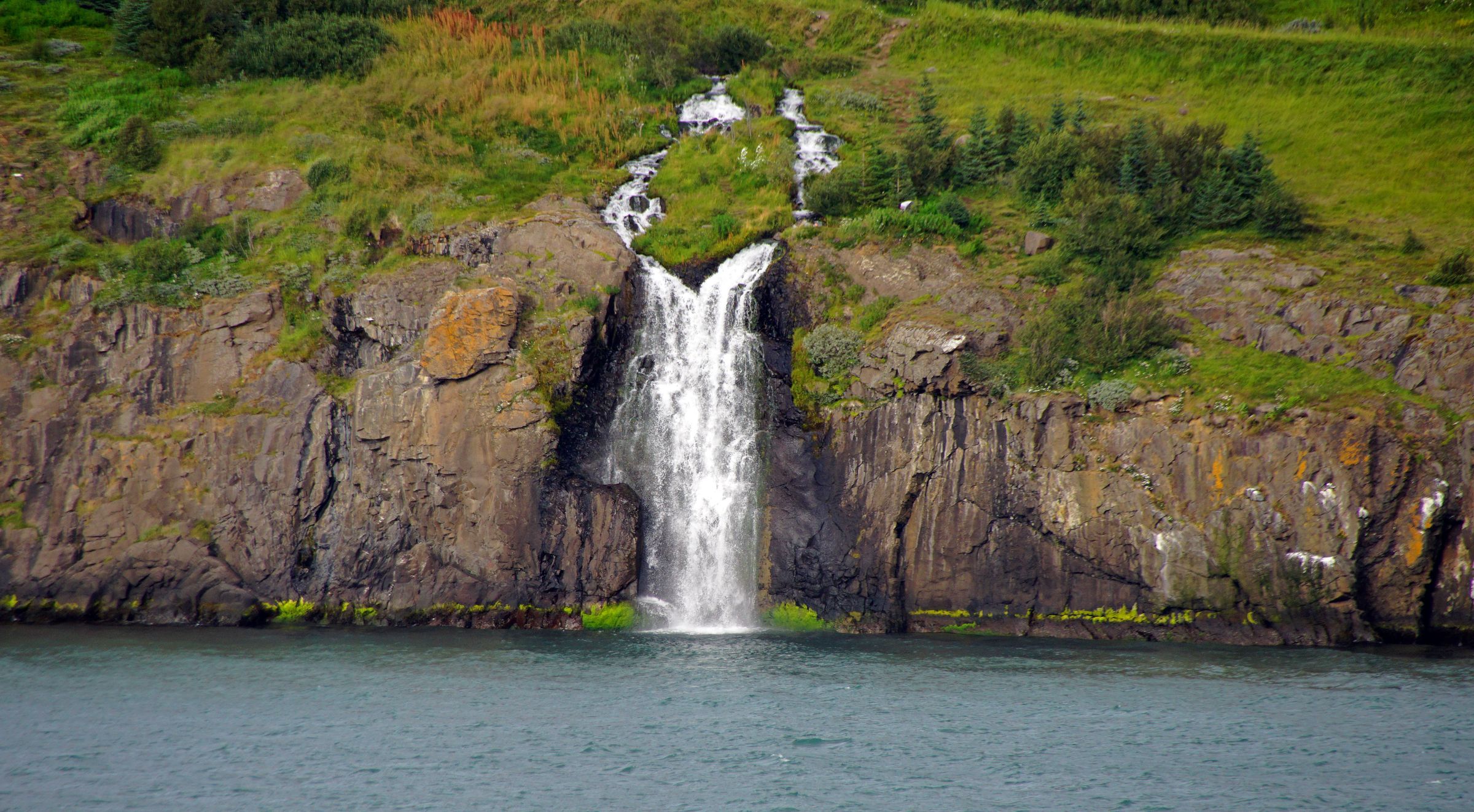 a waterfall is coming down a cliff into a body of water in Eyjafjörður by tröllaskagi in north iceland.