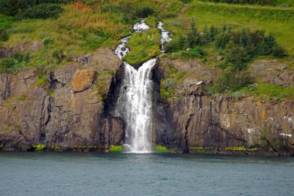 a waterfall is coming down a cliff into a body of water in Eyjafjörður by tröllaskagi in north iceland.