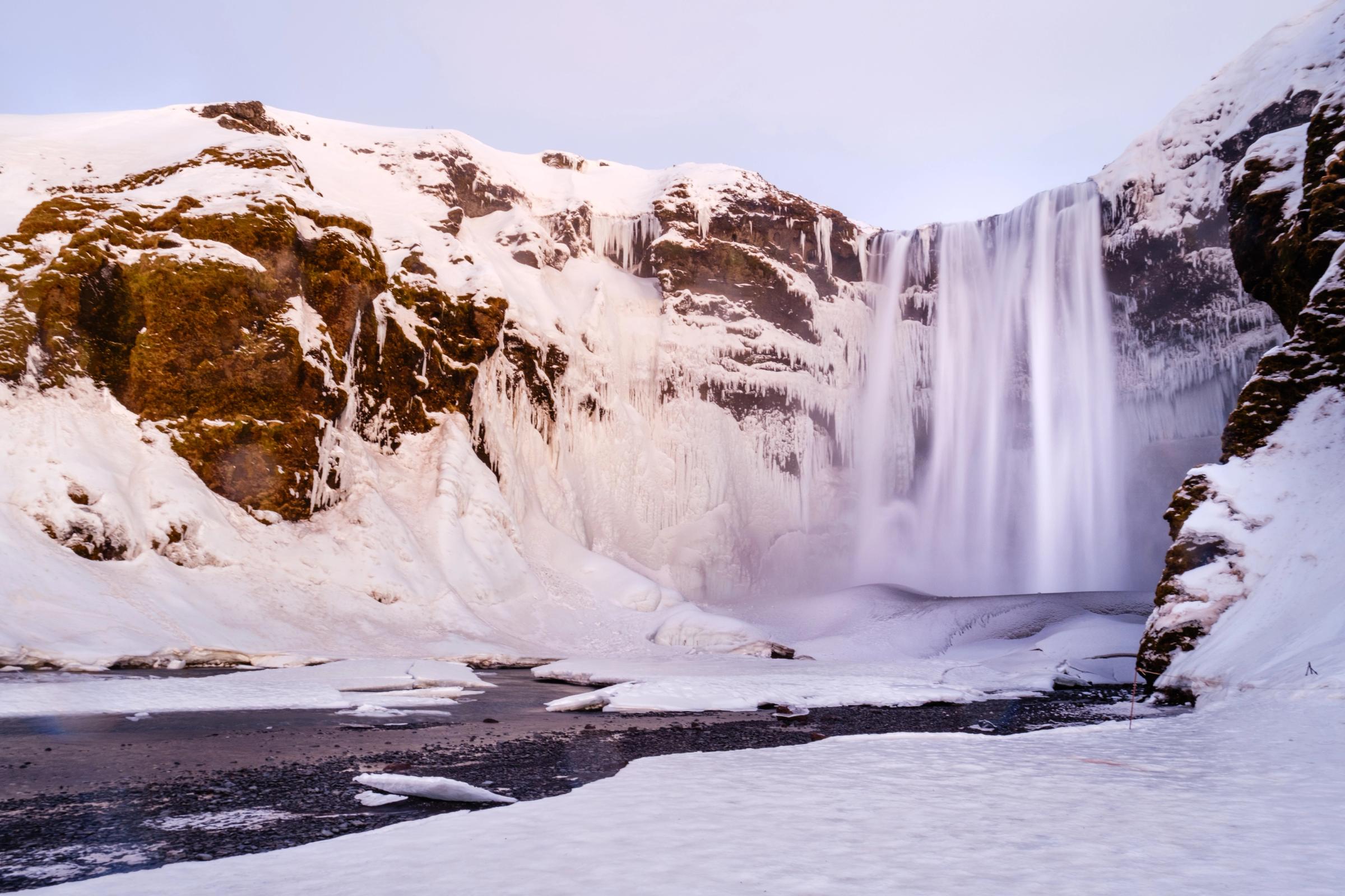 una cascada está rodeada de montañas cubiertas de nieve y un río .