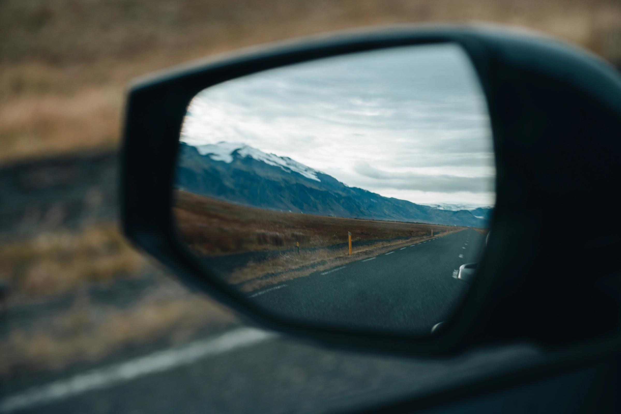 Hliðarspegill á Kia Sportage sem endurspeglar malbikaðan veg og fjöll á leiðinni