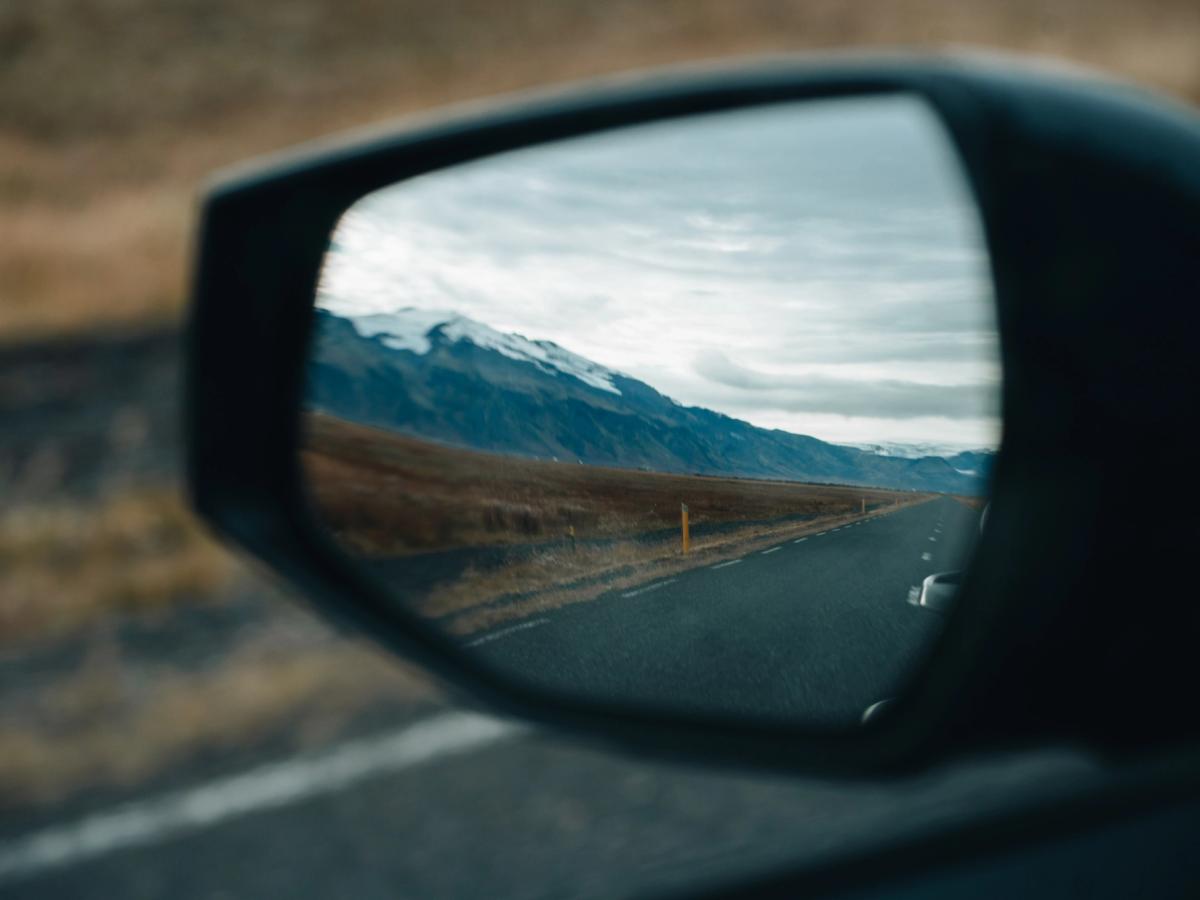 Spegilsýn Sportage Hliðarspegill á Kia Sportage sem endurspeglar malbikaðan veg og fjöll á leiðinni