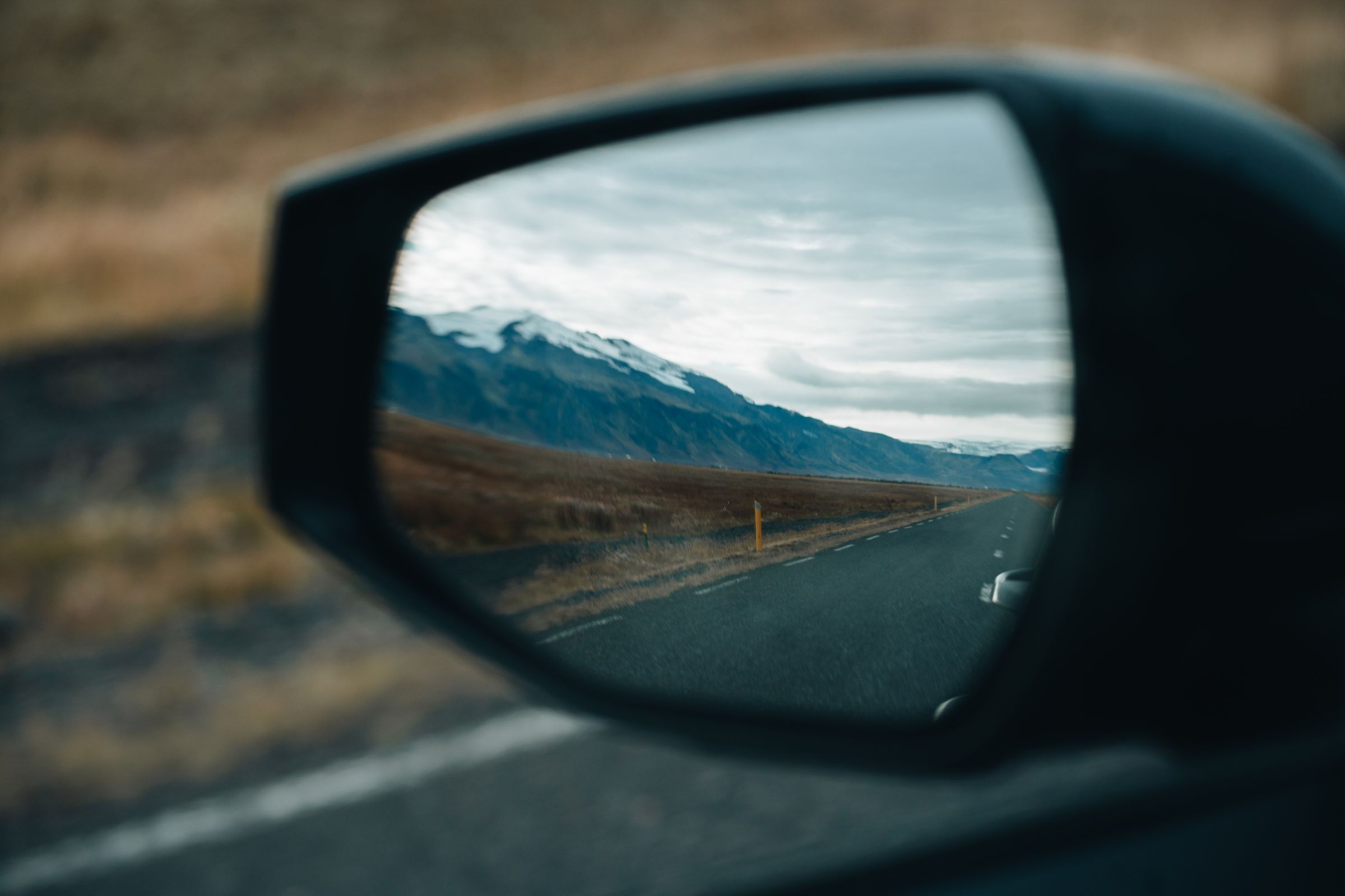 Spegilsýn Sportage Hliðarspegill á Kia Sportage sem endurspeglar malbikaðan veg og fjöll á leiðinni