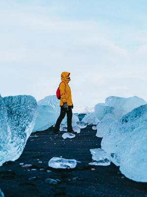 a person in a yellow jacket is walking through a pile of ice in iceland.
