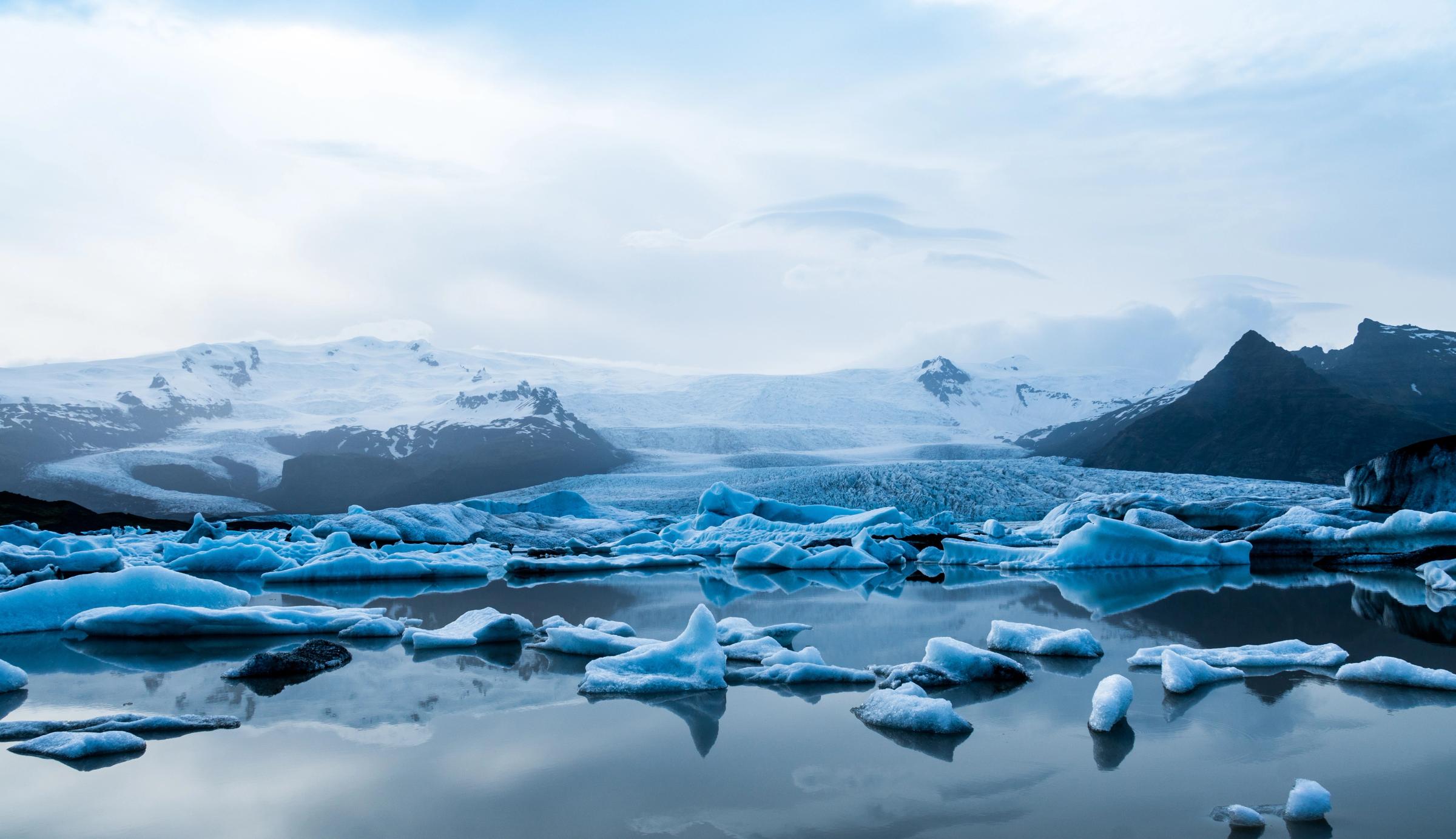 A glacial lagoon filled with icebergs, with snow-capped mountains and a glacier in the background.