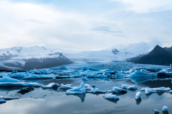 A glacial lagoon filled with icebergs, with snow-capped mountains and a glacier in the background.