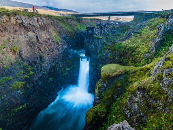 una cascada en el medio de un cañón con un puente al fondo .