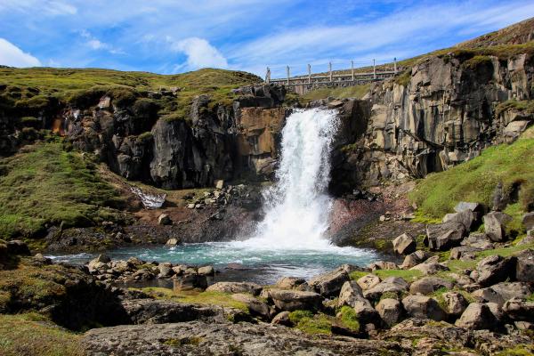 a waterfall is surrounded by rocks and grass on a hillside .