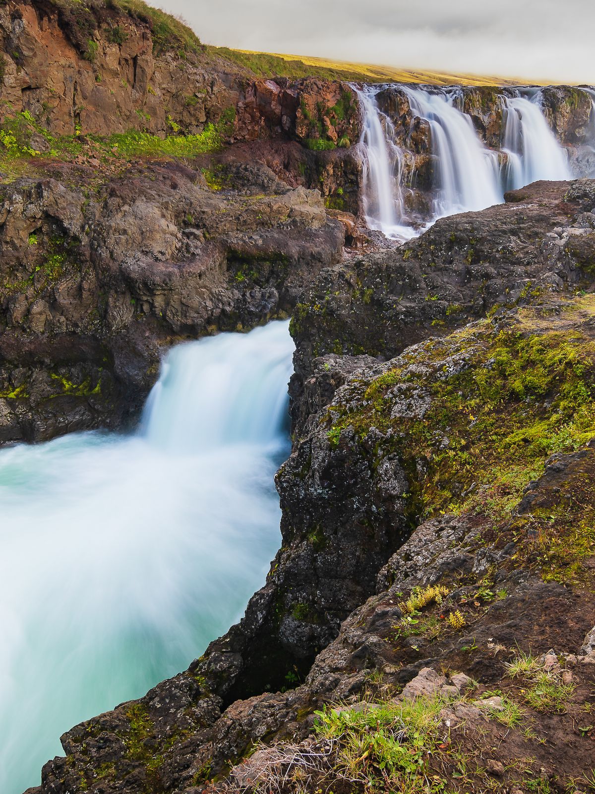 a waterfall in the middle of a canyon surrounded by rocks and grass .