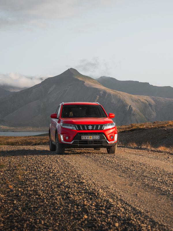Red SUV on a gravel road in a mountain landscape.