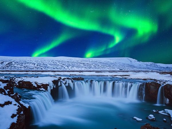 the aurora borealis is shining over a waterfall in iceland .