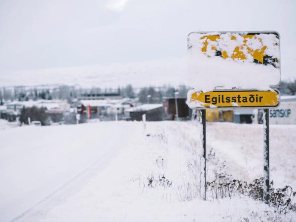 Snow-covered sign reading "Egilsstaðir" in a wintry landscape.