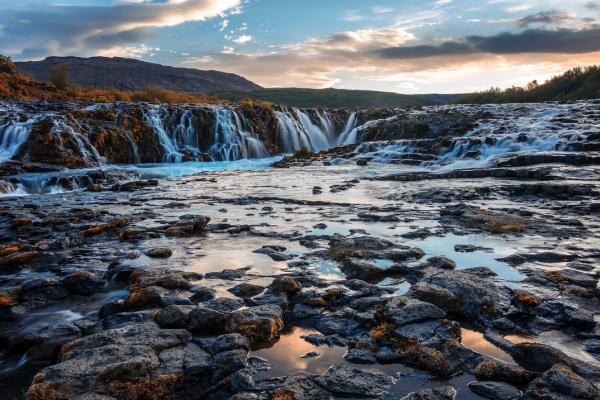 a waterfall is surrounded by rocks and mountains in the middle of a river in iceland.