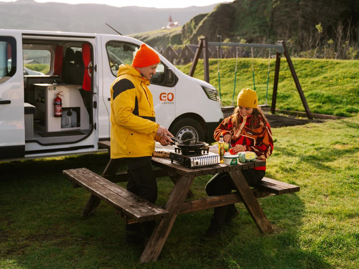 Un homme et une femme sont assis à une table de pique-nique devant une camionnette.